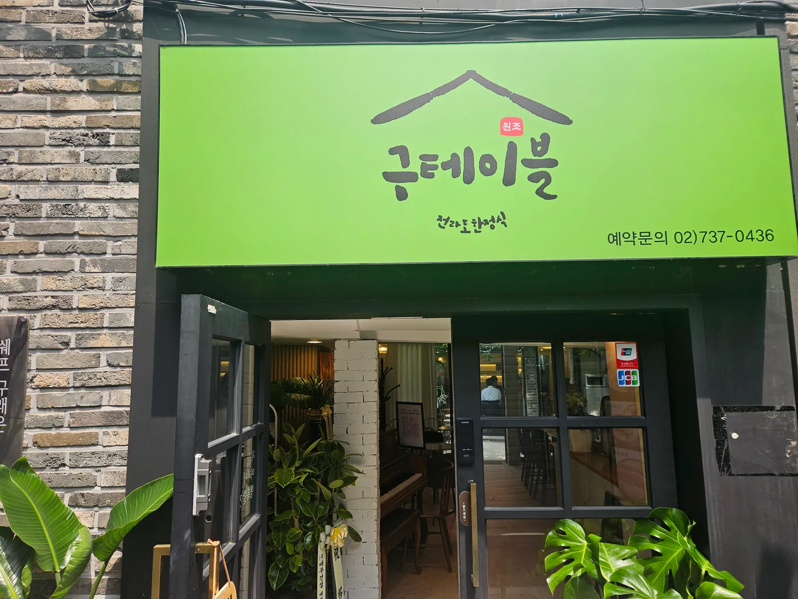 골목에서 본 구테이블 한정식 입구. 초록 간판에 「구테이블 전라도 한정식」과 예약 문의 전화번호가 적혀 있고, 유리문 안쪽으로 홀이 보인다.