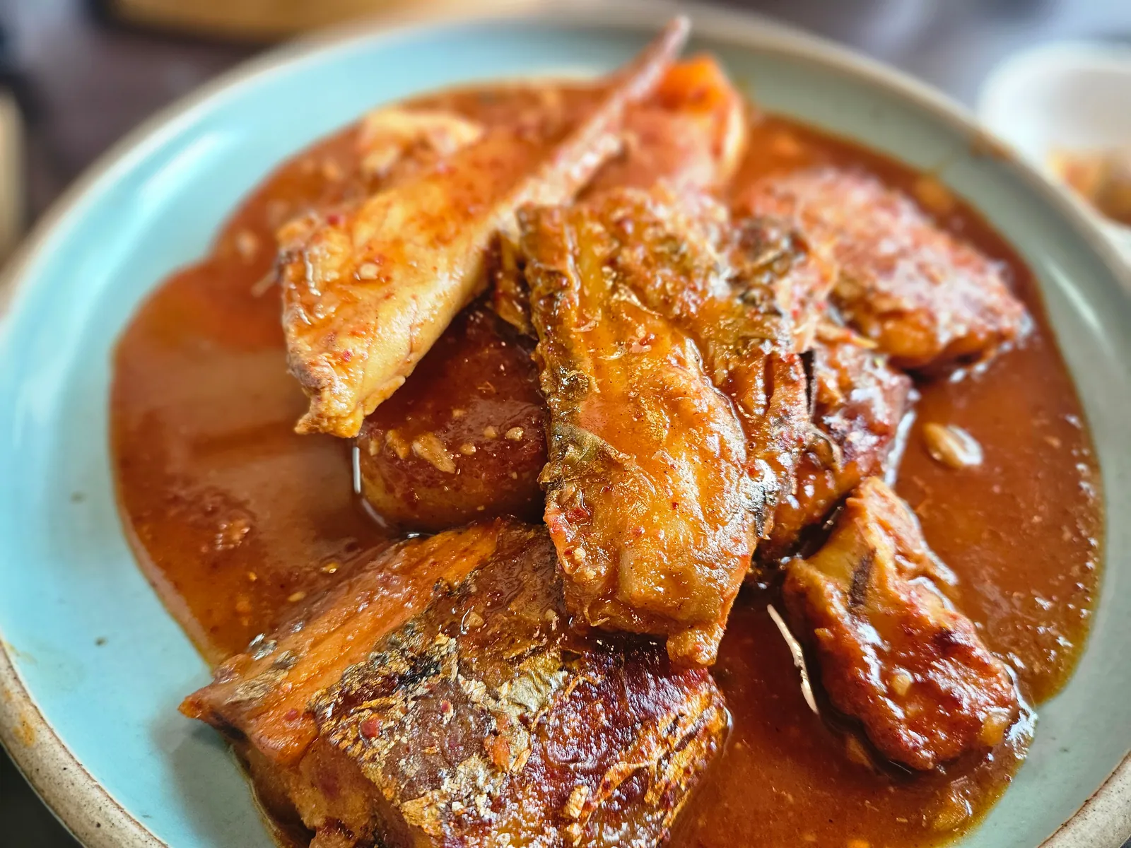 계절 생선조림. 붉은 양념 국물에 조린 생선 토막을 청록색 접시에 담았다.