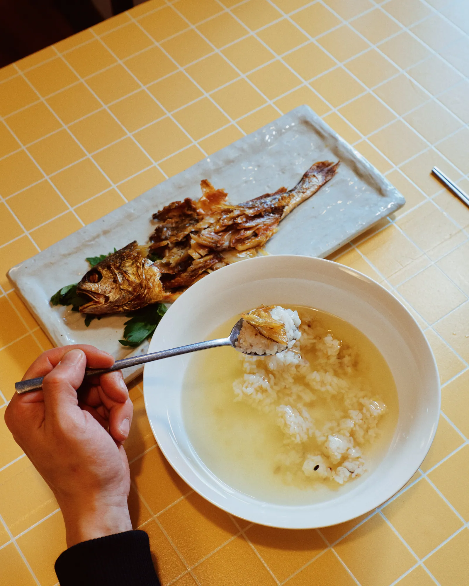 보리굴비정식. 길쭉한 접시에 구운 굴비가 놓이고, 옆 대접에는 맑은 국물에 만 밥을 숟가락으로 뜨고 있다.